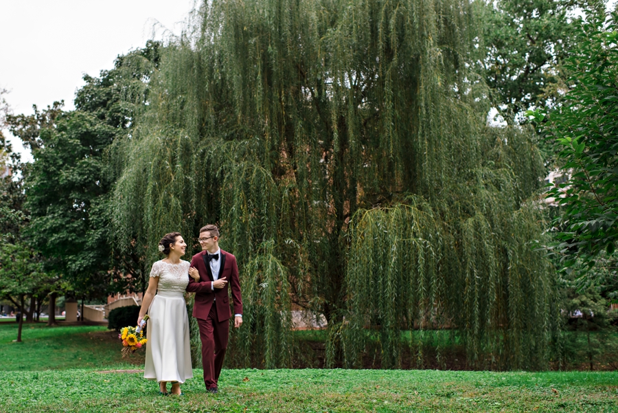 A bride and groom hold each other while walking in front of a large weeping willow tree in Philly.